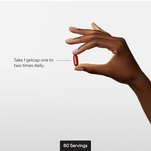 Hand holding a red gelcap with dosage instructions.