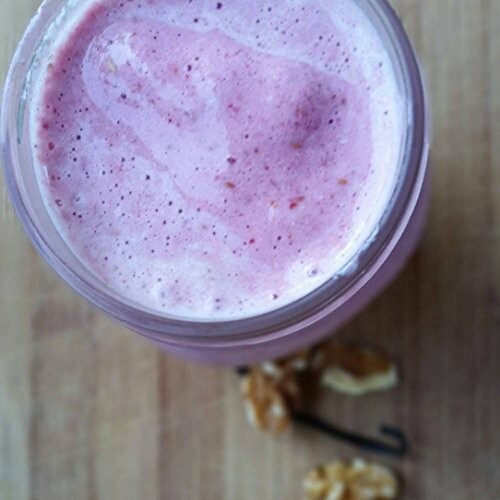 Top view of a pink smoothie in a jar on a wooden surface with walnuts nearby.